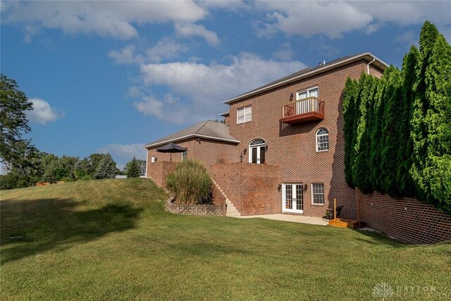 back of property featuring a balcony, a yard, and french doors