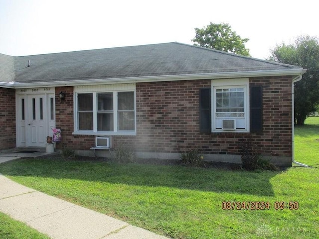 view of front of property with a wall mounted air conditioner and a front yard