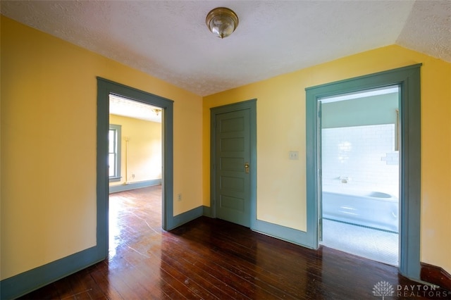 spare room featuring a textured ceiling, dark wood-type flooring, and lofted ceiling