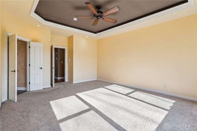 empty room with a raised ceiling, ceiling fan, light carpet, and ornamental molding