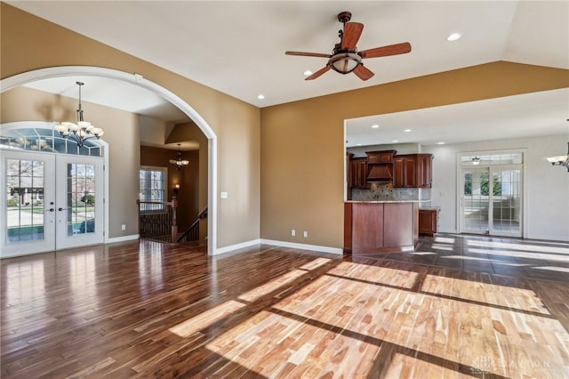 unfurnished living room featuring dark hardwood / wood-style flooring, french doors, ceiling fan with notable chandelier, and plenty of natural light