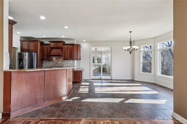 kitchen with stainless steel fridge with ice dispenser, premium range hood, a wealth of natural light, and a chandelier