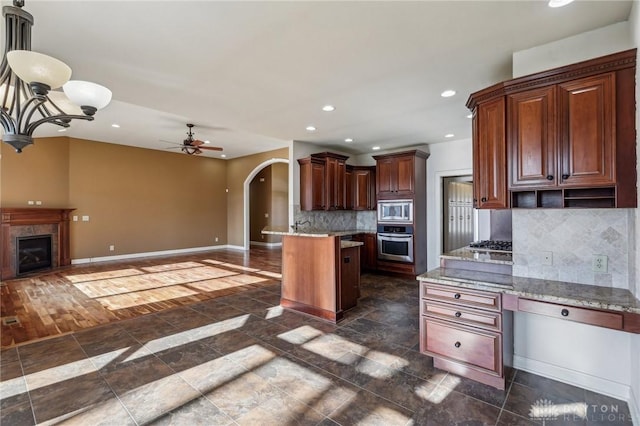 kitchen with backsplash, a tile fireplace, ceiling fan, appliances with stainless steel finishes, and a kitchen island