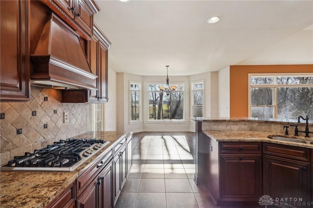 kitchen with custom range hood, stainless steel gas cooktop, a healthy amount of sunlight, sink, and an inviting chandelier