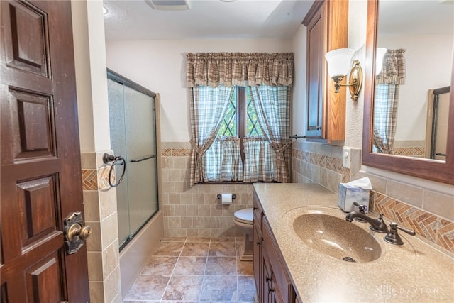 full bathroom with shower / bath combination with glass door, vanity, toilet, and tile walls