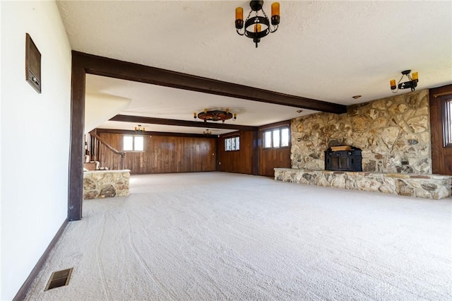 unfurnished living room featuring beam ceiling, light colored carpet, wooden walls, and a healthy amount of sunlight