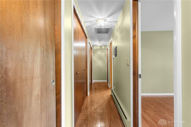 corridor with a baseboard heating unit and hardwood / wood-style floors