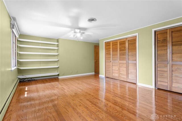 unfurnished bedroom featuring a baseboard heating unit, multiple closets, ceiling fan, and light hardwood / wood-style floors