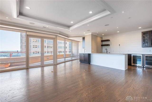 unfurnished living room with dark wood-type flooring, a tray ceiling, wine cooler, and wet bar