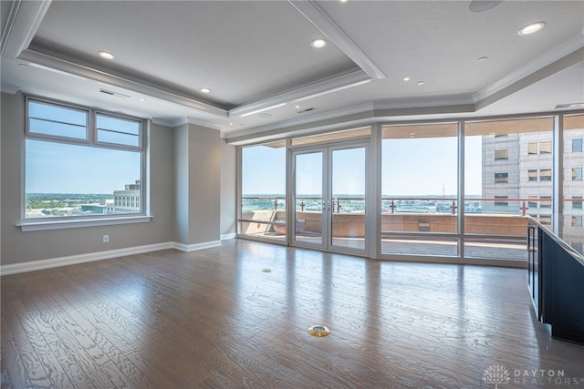 empty room featuring a tray ceiling, a view of city, crown molding, wood finished floors, and baseboards