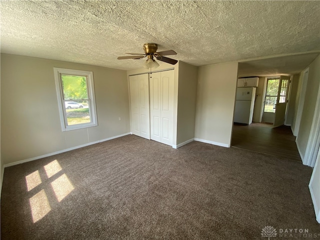 unfurnished bedroom with a textured ceiling, a closet, dark colored carpet, ceiling fan, and white refrigerator