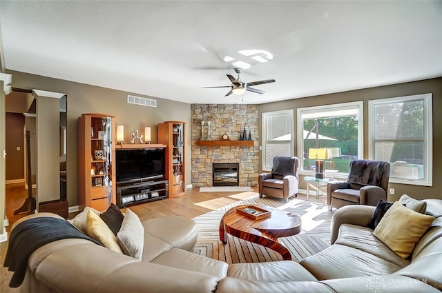 living room featuring ceiling fan, light hardwood / wood-style floors, and a stone fireplace