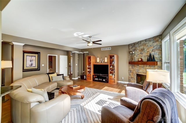 living room featuring ceiling fan, wood-type flooring, and a stone fireplace