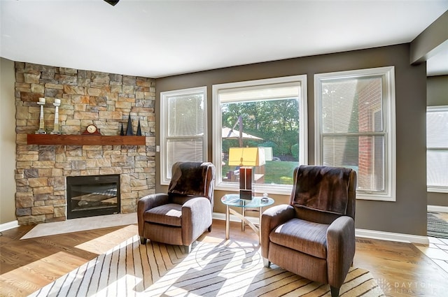 sitting room with a stone fireplace and light wood-type flooring