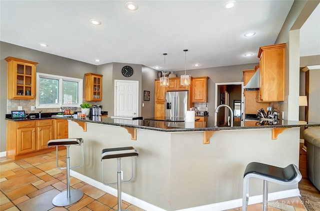 kitchen with pendant lighting, dark stone counters, backsplash, kitchen peninsula, and stainless steel fridge with ice dispenser