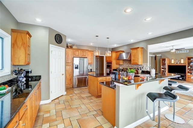 kitchen with decorative light fixtures, wall chimney range hood, ceiling fan, a kitchen island, and stainless steel fridge with ice dispenser