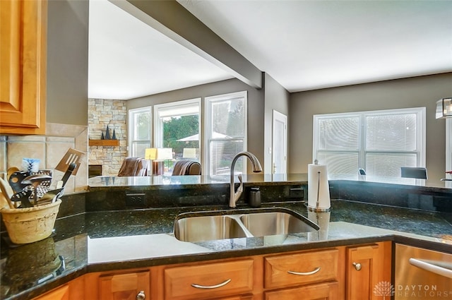 kitchen featuring sink, a stone fireplace, beamed ceiling, and dark stone counters