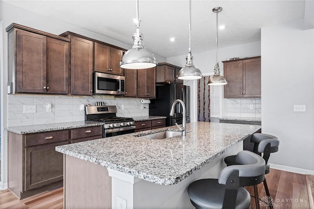 kitchen featuring a kitchen bar, backsplash, an island with sink, appliances with stainless steel finishes, and light hardwood / wood-style floors