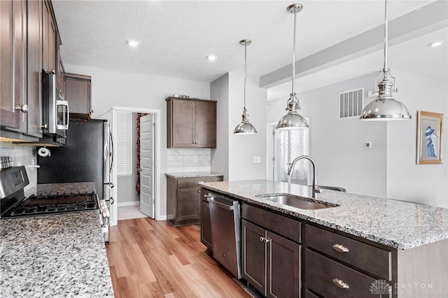 kitchen with backsplash, hanging light fixtures, stainless steel appliances, sink, and a kitchen island with sink