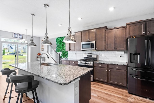 kitchen featuring light hardwood / wood-style flooring, decorative light fixtures, stainless steel appliances, an island with sink, and light stone countertops