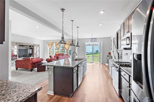 kitchen featuring dark stone counters, dark brown cabinets, stainless steel appliances, plenty of natural light, and an island with sink