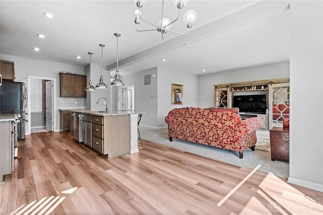 kitchen with light hardwood / wood-style flooring, light stone counters, sink, hanging light fixtures, and a center island with sink