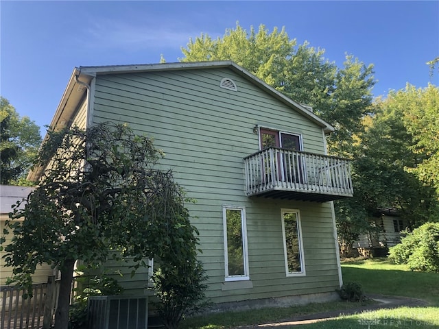 view of side of property featuring a lawn, a balcony, and central AC