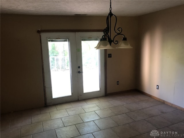 unfurnished dining area featuring an inviting chandelier, french doors, and a textured ceiling