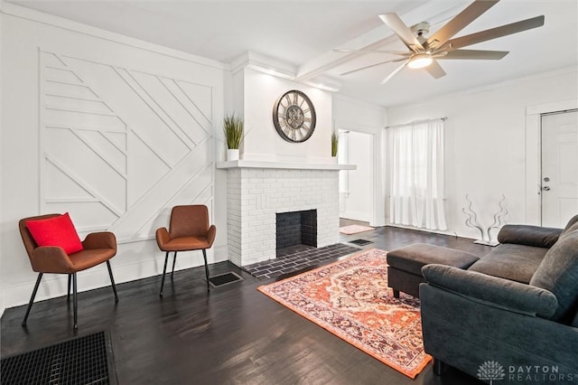 living room featuring dark wood-type flooring, ornamental molding, beamed ceiling, ceiling fan, and a fireplace