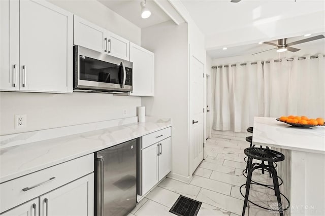 kitchen with white cabinetry, ceiling fan, appliances with stainless steel finishes, and light stone countertops