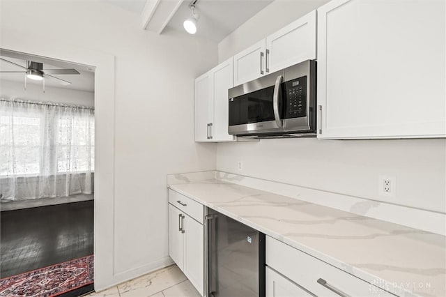 kitchen with white cabinetry, light stone counters, track lighting, and ceiling fan