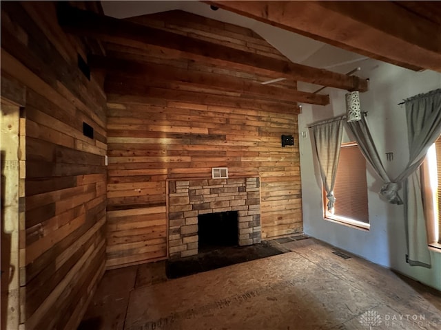 unfurnished living room with wood walls, a stone fireplace, and beam ceiling