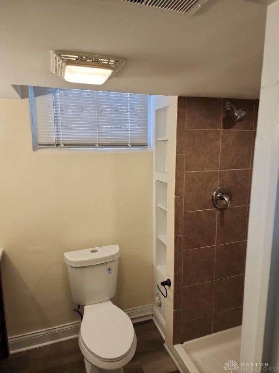 bathroom with wood-type flooring, toilet, and a tile shower