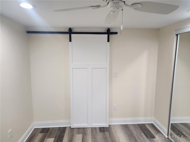 unfurnished bedroom with ceiling fan, a barn door, a closet, and dark hardwood / wood-style flooring