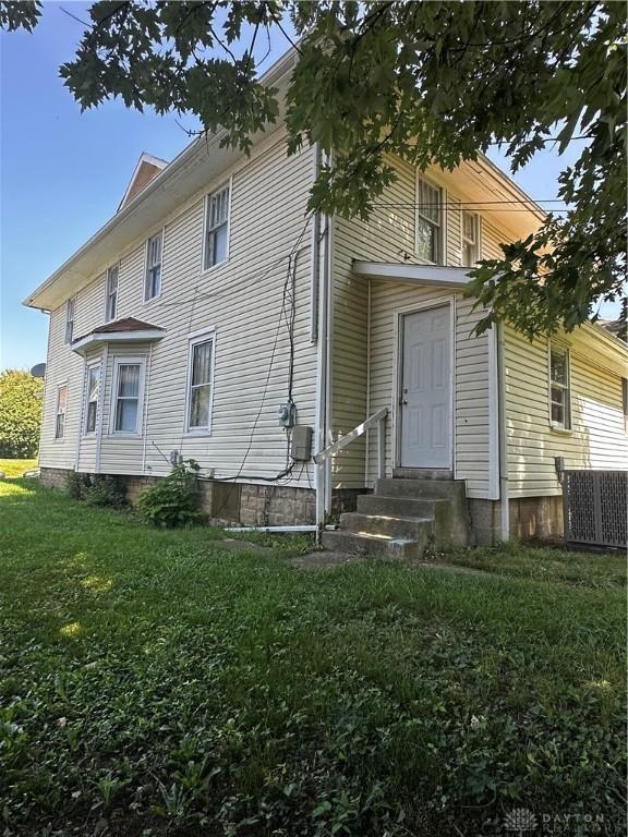 view of front facade featuring entry steps, central air condition unit, and a front yard