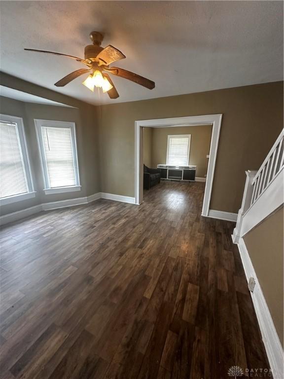 unfurnished living room with ceiling fan, dark hardwood / wood-style floors, and a textured ceiling