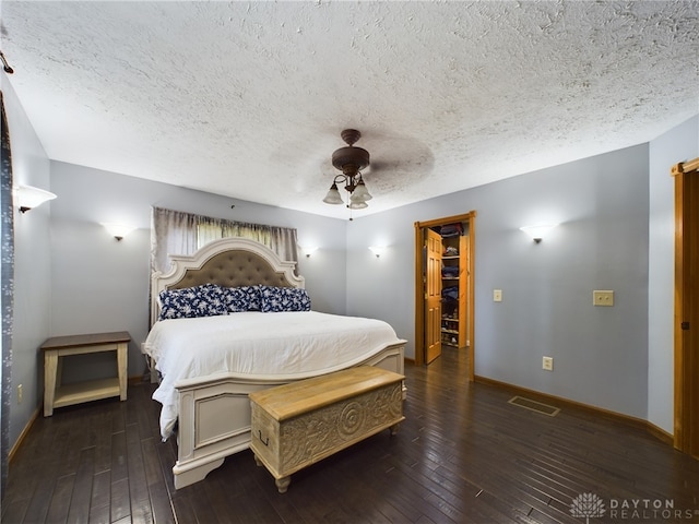 bedroom featuring ceiling fan, dark hardwood / wood-style floors, a spacious closet, and a textured ceiling