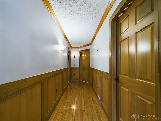 hallway featuring ornamental molding, a textured ceiling, and light hardwood / wood-style floors