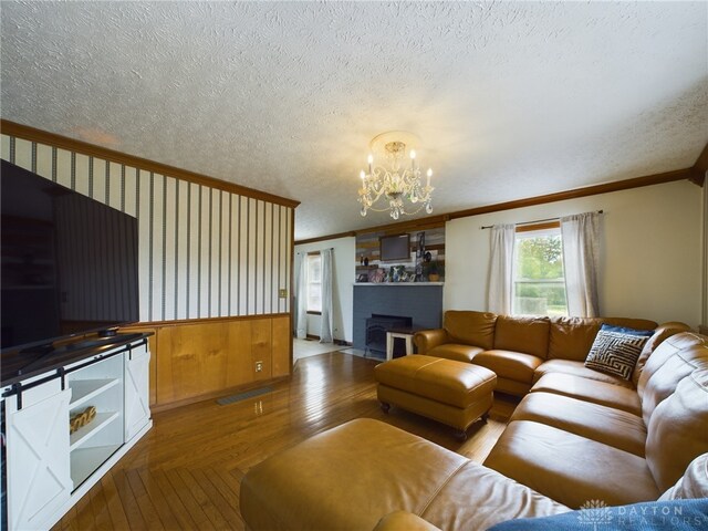 living room with a textured ceiling, ornamental molding, wooden walls, and a chandelier