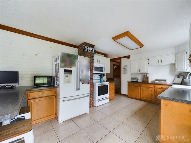 kitchen with a textured ceiling, light tile patterned floors, white appliances, and wooden walls