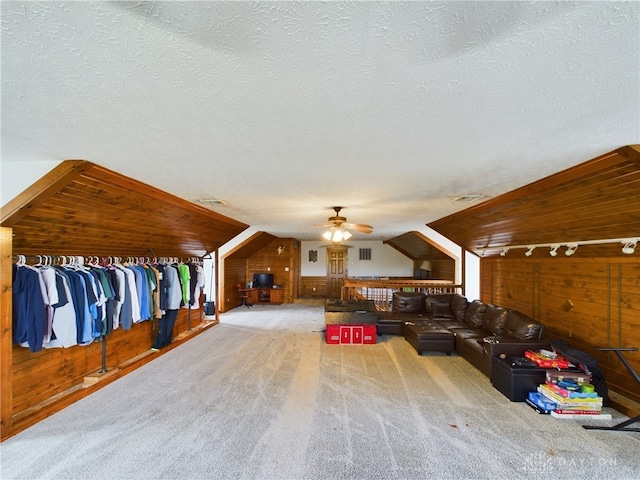 interior space featuring carpet flooring, ceiling fan, wooden walls, and a textured ceiling