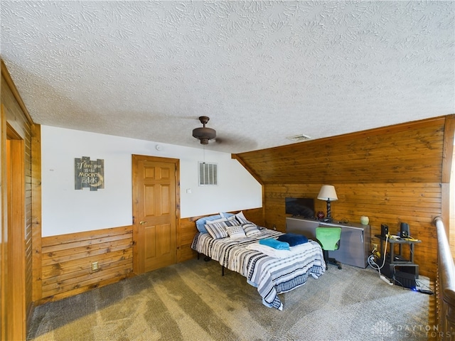 bedroom with a textured ceiling, carpet, wood walls, and ceiling fan