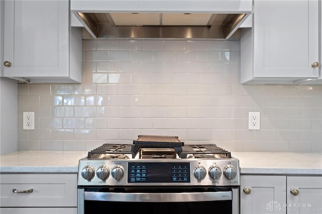 kitchen with light stone countertops, stainless steel stove, decorative backsplash, wall chimney range hood, and white cabinets