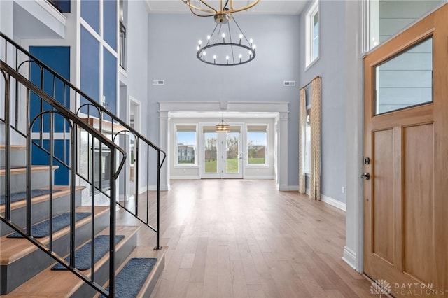 entryway featuring light wood-type flooring, a towering ceiling, and an inviting chandelier