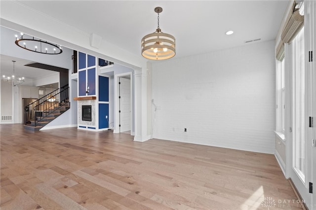 unfurnished living room featuring hardwood / wood-style floors, a notable chandelier, and brick wall