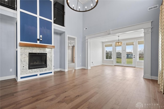 unfurnished living room with a towering ceiling, hardwood / wood-style flooring, a premium fireplace, and a chandelier