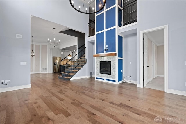 unfurnished living room with crown molding, a high ceiling, an inviting chandelier, and hardwood / wood-style flooring