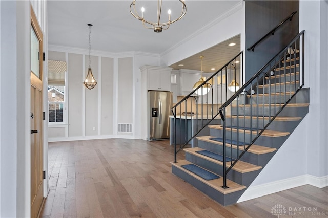 entryway with ornamental molding, hardwood / wood-style flooring, and an inviting chandelier