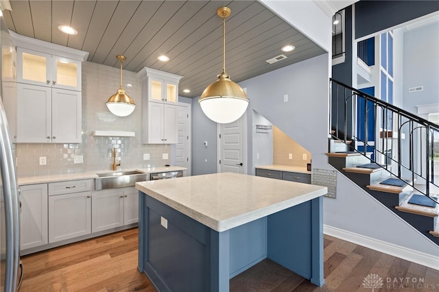 kitchen with hanging light fixtures, wood-type flooring, white cabinets, and tasteful backsplash