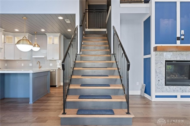 stairs featuring a towering ceiling, wood-type flooring, a high end fireplace, and sink